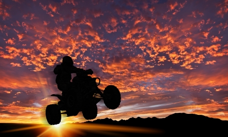 dramatic background sky with quad bike rider silhouetted against setting sunの写真素材