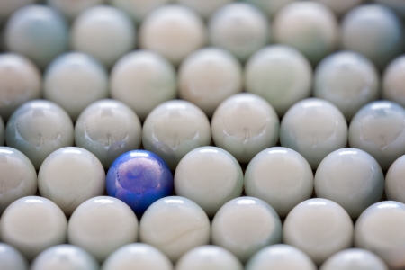 pale opal marbles displayed with one blue marble standing out as abstractの写真素材
