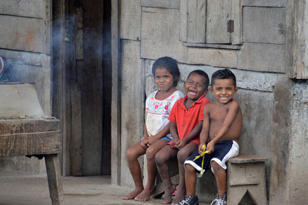 SAUPUKA, NICARAGUA - JULY 8, 2015:  Two unknown Nicaraguan boys and one unknown Nicaraguan girl sit on their porch playing under cover during a slight rain.のeditorial素材