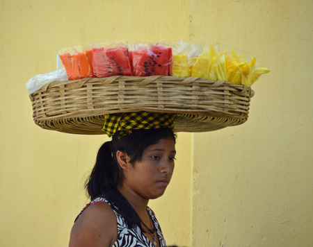 ANTIGUA, GUATEMALA - JUNE 27, 2015; An unknown, young Guatemalan woman carries sliced fruit in a basket on her head.  She walks the local streets selling to locals and tourists.のeditorial素材