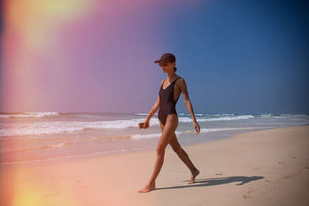 Beautiful girl walk on beach on ocean with phoneの写真素材