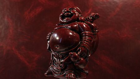 Hotei - God of Contentment and Happiness. Japanese Buddhism. Figurine, almost merging with a burgundy background.の写真素材