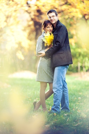 Lovers spend sunny day in the autumn park, they hold a bouqet of autumn leaves; blurs around themの写真素材