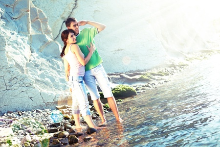 Young couple on the rocky coast standing ankle-deep in water and looking over the horizonの写真素材