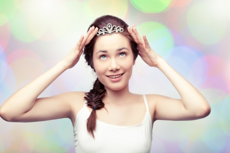 Beautiful girl is putting on a diamond diadem and admiring it, colorful pastel backgroundの写真素材