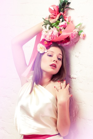 Beautiful young woman / bride in white dress holding bouquet of peonies lean against the wallの写真素材