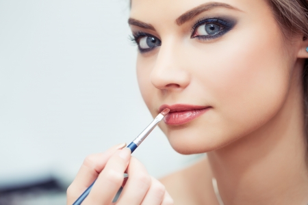 Make-up artist applying lipstick with a brush on model s lips, close-up, model looking at cameraの写真素材