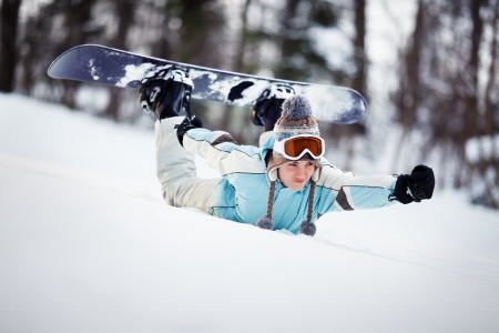 Young female snowboarder sliding down the slope on her belly, holding her hand out in front of herの写真素材