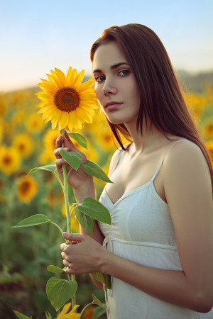 Portrait of young woman holding sunflower on summer fieldの写真素材