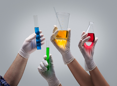 Chemist hands in latex gloves holding laboratory glassware with liquids on light grey background
