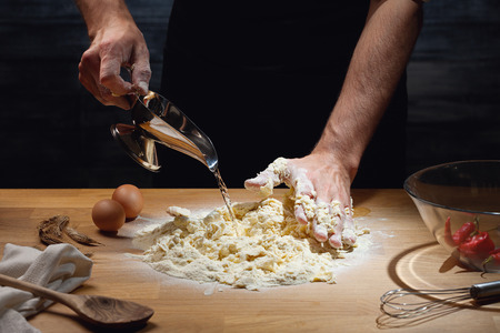 Cook hands kneading dough, adding water to flour. Low key shot, close up on hands, some ingredients around on table.の写真素材