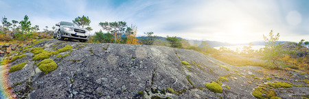 Panoramic view of norwegian rocks and distant fjord, car parked on the top; lense flare.