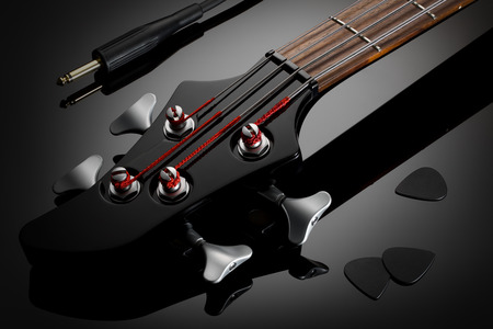 Close up on the black headstock of electric bass guitar, black picks and jack cable next to it....