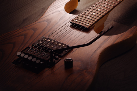 Close up on the body of custom electric guitar with natural finish, selective light on it, wooden...
