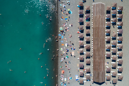 Top aerial view of the pebble beach. Rows of umbrellas and sunbeds, warm blue sea and holiday makers having fun. Copy spaceの写真素材