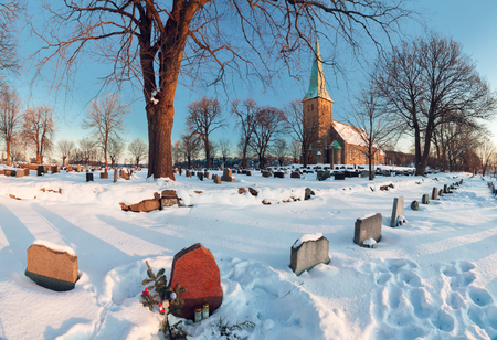 Winter landscape with a norwegian countryside church at sunset, graveyard on foregroundの写真素材