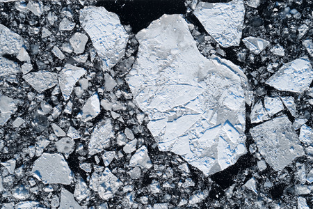 Top aerial view of cracked ice floating in dark water