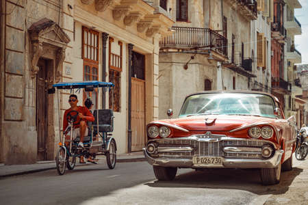 Havana, Cuba - March 22, 2019: Shiny retro car parked on the street and bicycle taxi driver riding byのeditorial素材