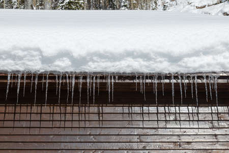 Wooden cabin with snowy roof and icicles at sunny winter day, close up