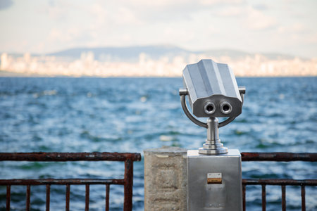 Public binoculars on the seaside promenade overlooking a distant city.の写真素材