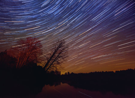 A long exposure of the sky over a lake with the star trailsの写真素材