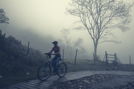 Cyclist on the countryside road surrounded with milky fog. Mexico, Huasteca Potosina, Aquismon