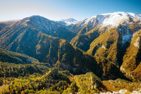 Panoramic view of the Caucasus mountains with snow-covered peaks and colorful autumn forests.
