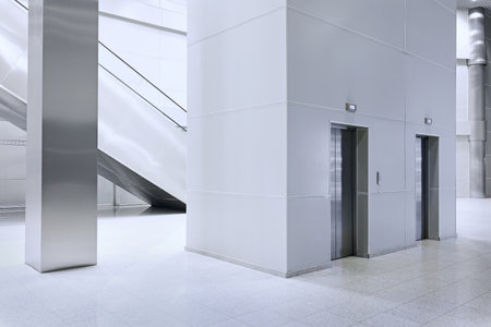 Clean, minimalist public interior two features stainless steel elevator entrances set in a light...