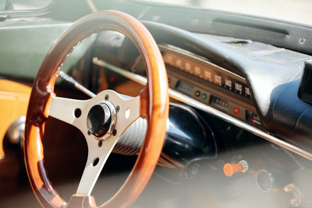 Close-up of a vintage car's interior, showing the glossy wood and metal steering wheel near the dashboard panel.の写真素材