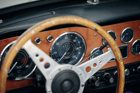 Close-up on the interior of a classic open-top car, featuring a wood-rimmed wheel, speedometer, and other gauges on a wooden dashboard.の写真素材