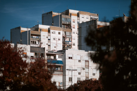 Residential brutalist building in New Belgrade with balconies framed by trees against a clear blue sky.の写真素材