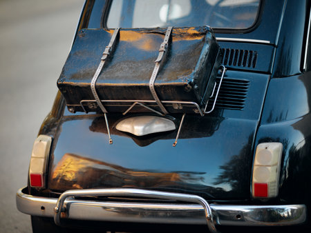 Rear view of a black vintage car with a luggage rack and an old suitcase strapped on it.の写真素材