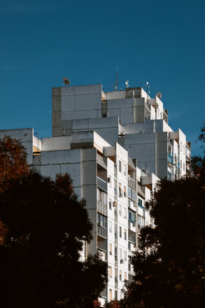 Residential brutalist building in New Belgrade with balconies framed by trees against a clear blue...