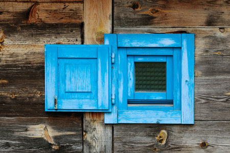 Small window with a painted blue frame on a rustic weathered wood wall.の写真素材