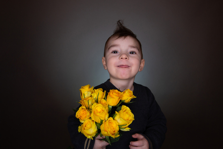 Cute boy with yellow roses, bouquet of flowers, gives present with copy spaceの写真素材