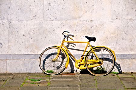 Yellow bicycle with flat tyres, leaning against a marble wall in Pisa, Italy.の写真素材