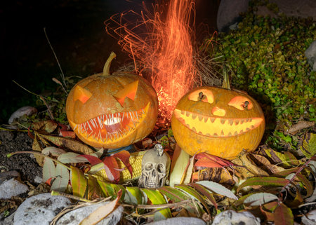 carved pumpkins surrounded by sparks, smoke and fire, Halloween composition with smiling pumpkins and Halloween accessories, corn cobs, skull, Halloween party in autumn, carved pumpkinの写真素材