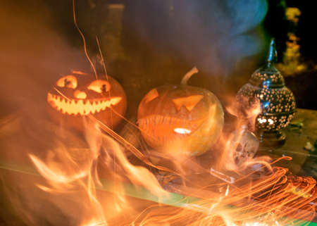 carved pumpkins surrounded by sparks, smoke and fire, Halloween composition with smiling pumpkins and Halloween accessories, corn cobs, skull, Halloween party in autumn, carved pumpkinの写真素材