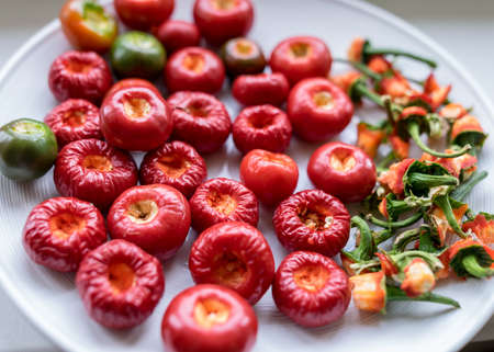 picture with tomato peppers on a white plate, peppers prepared for canning, green stalks separated, concept of healthy eating, vegetarian diet, canning products for winter, autumn harvest timeの写真素材