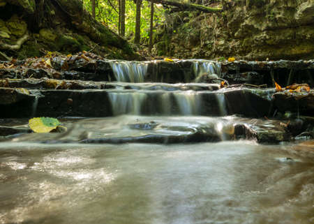 a small rapid river flows through dolomite rocks, long-term exposure, gentle and fuzzy river water, colorful autumn leaves and dry branches in the riverの写真素材