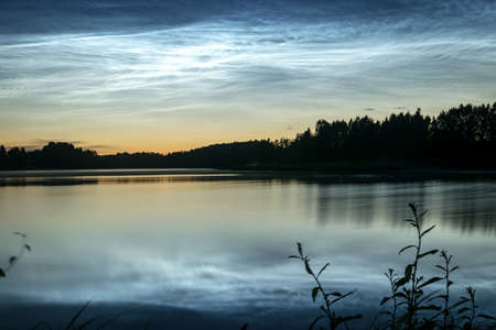 beautiful night landscape with white silver clouds over the lake, blurred foreground, charming cloud reflections in the lake water, summer nightの写真素材
