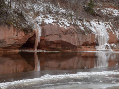 landscape with sandstone cliff and icicles, white iceberg on red wall, reflections in riverの写真素材