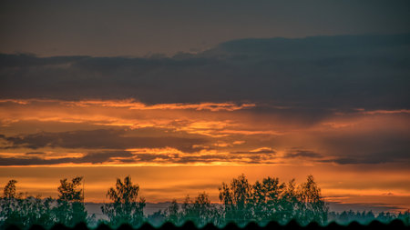 summer landscape with a colorful sunset over the roof, view through the windowの写真素材