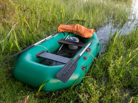 summer landscape with a green rubber boat on the lake shore, fishing tackleの写真素材