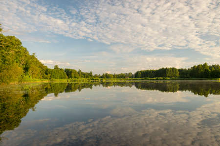beautiful summer morning landscape on the lake, beautiful clouds and wonderful reflections in the lake mirror, summer morning by the waterの写真素材