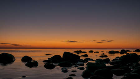 orange sunset by the sea, black stone silhouettes against the sea background, summer eveningの写真素材