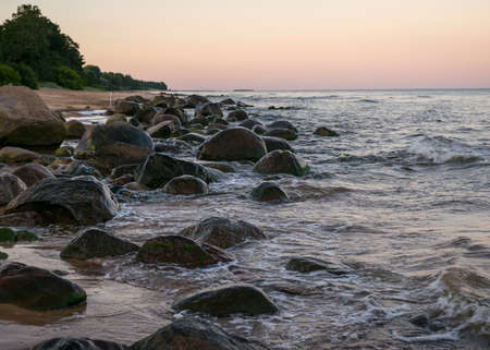 rocky sea shore before sunrise, dark stone silhouettes and colorful sky, Baltic Sea coast, Latviaの写真素材