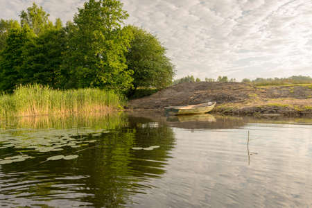 view of the boat on the shore of the lake, reflections in the calm water of the lake, summer morningの写真素材