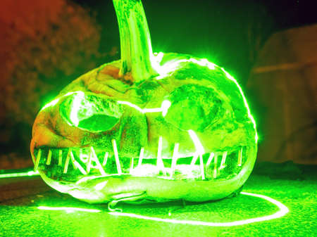terrible a burning carved pumpkin with a scary face and colorful light drawings in a dark background, suitable for Halloweenの写真素材