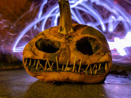 terrible a burning carved pumpkin with a scary face and colorful light drawings in a dark background, suitable for Halloweenの写真素材